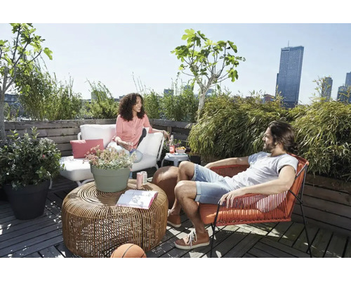 Een zonnige daktuin met zitplaatsen, planten en twee mensen.