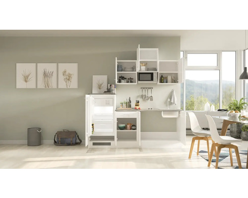 Compacte keuken met koelkast, spoelbak, magnetron en opbergruimte in een lichte ruimte.