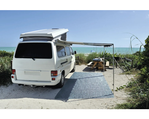 Witte camper met luifel en picknickplaats op het strand.