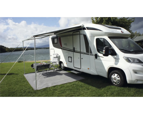 Camper met luifel, tafel, stoelen en grondbeschermingsmat op een grasveld aan een meer