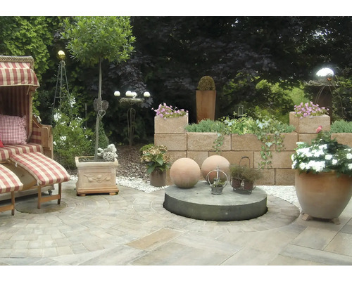 Aangelegde tuin met strandstoel, muur en plantenbakken.