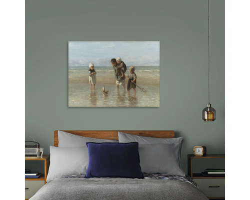Schilderij aan de muur boven een bed met een scène van kinderen op het strand.