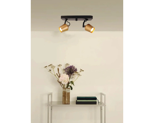 Plafondlamp met twee spots in gouden look en zwarte houder boven een rek met decoratie