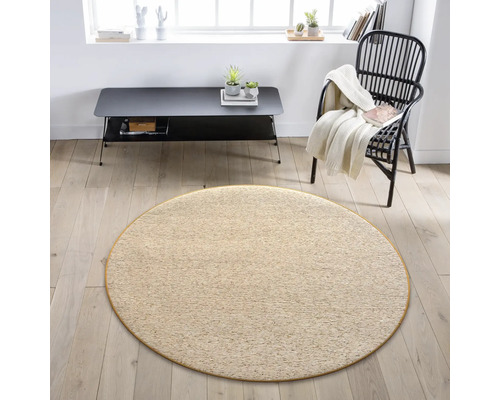 Beige rond tapijt in een woonkamer met fauteuil en tafel