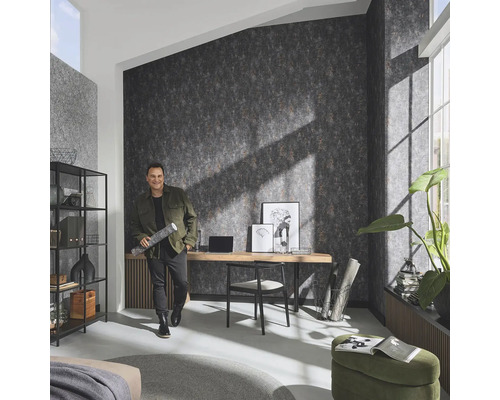 Woonkamer met patroonbehang, bureau en man met behangrol