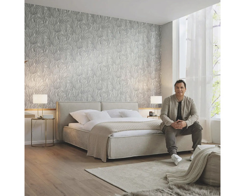 Lichte slaapkamer met behang met patroon, tweepersoonsbed, vloerkleed en zittende man