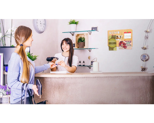 Een klant betaalt met een creditcard bij de kassa, op de achtergrond een kurk prikbord