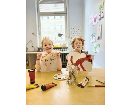 Twee kinderen tonen hun met verf geschilderde schilderijen aan tafel, omringd door verftubes en penselen