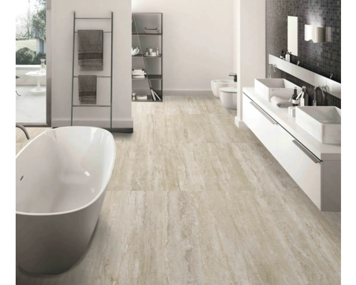 Lichte badkamer met ligbad, wastafel, toilet en vloertegels in natuursteenlook.