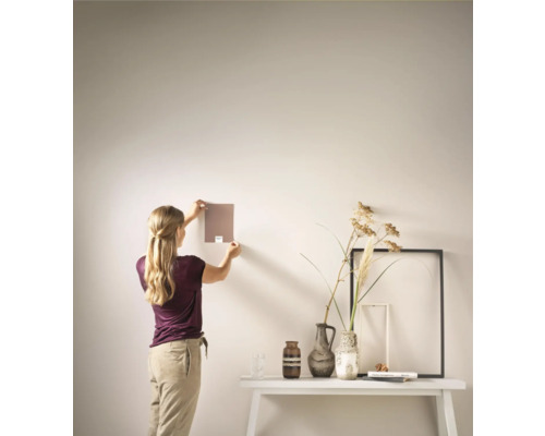 Vrouw houdt kleurstaal tegen de muur boven een dressoir met decoratie.