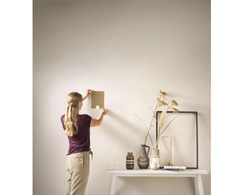 Vrouw houdt kleurstaal tegen de muur, arrangement met vazen en fotolijsten op tafel.