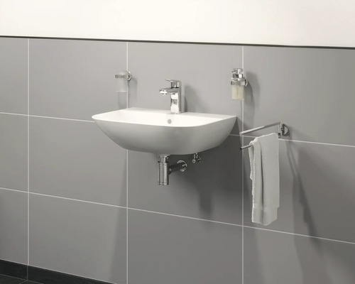 Keramische wastafel met kraan, zeepdispenser en handdoekhouder aan een betegelde muur