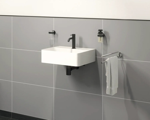 Hangende wastafel met kraan, zeepdispenser, tandenborstelbeker en handdoekhouder aan een muur