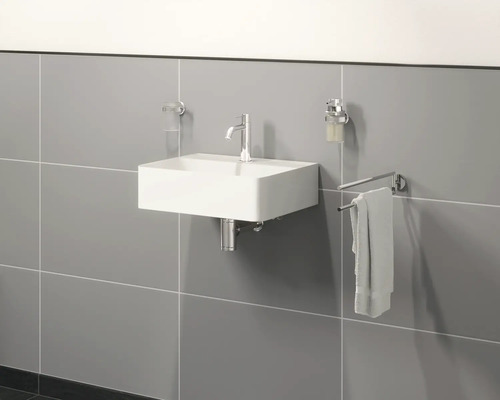 Wastafel aan de wand met kraan, zeepdispenser, handdoek en beker voor tandenborstels in een badkamer