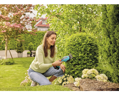 Vrouw snoeit struiken met een accustruikenschaar in de tuin.