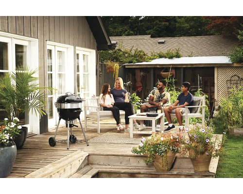 Familie ontspant op het terras met kogelbarbecue en tuinmeubelen
