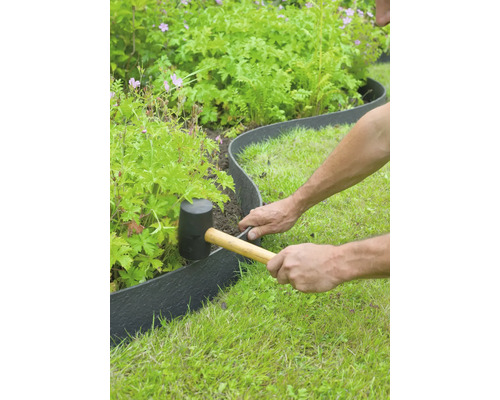 Een persoon installeert met een rubberen hamer een kunststof gazonrand in de tuin.