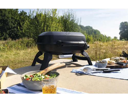 Zwarte draagbare gasbarbecue op een tafel met eten buitenshuis