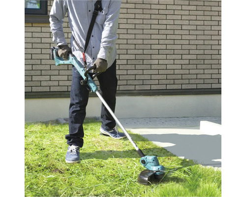 Een persoon gebruikt een accu grastrimmer in de tuin om gras te maaien.