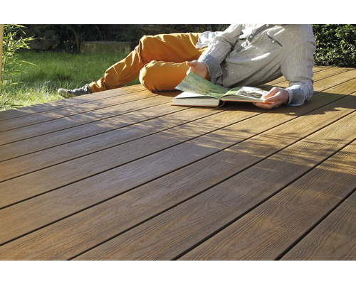 Persoon ligt op een houten terras en leest een boek.