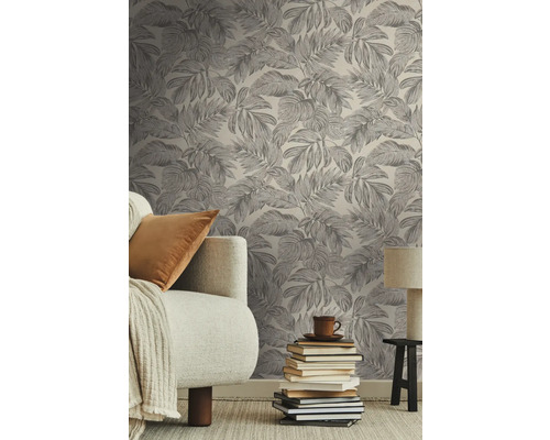 Woonkamer met een behang bedrukt met bladeren, een bank, een stapel boeken en een lamp.