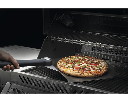 Pizza wordt met een pizzaschep op een grill gelegd.