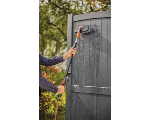 Een persoon reinigt een houten schutting met een borstel en een slang.