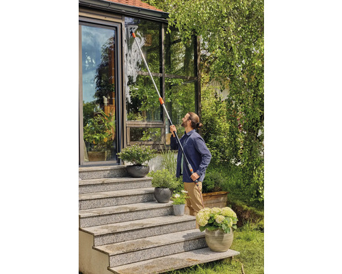 Man reinigt ramen van een serre met een raamwisser en telescopische steel.