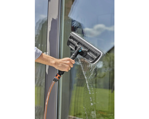 Een persoon reinigt een raam met een raamwisser en een waterslang.