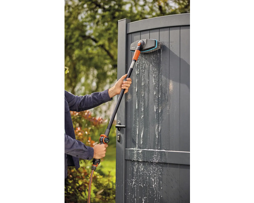 Persoon reinigt een tuinpoort met een wasborstel met telescopische steel