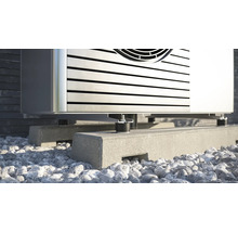 Detailopname van een warmtepomp op een betonnen sokkel met stenen ondergrond