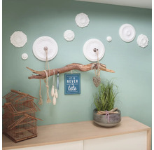 Decoratieve wanddecoratie met bloemmotieven, een tak als kapstok, een decoratie met een wijsheid en een decoratie op een commode met kooi en plant