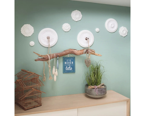 Decoratieve wanddecoratie met bloemmotieven, een tak als kapstok, een decoratie met een wijsheid en een decoratie op een commode met kooi en plant