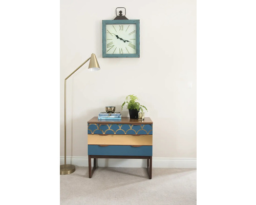 Decoratieve scène met een nachtkastje met drie laden, een vloerlamp en een wandklok.