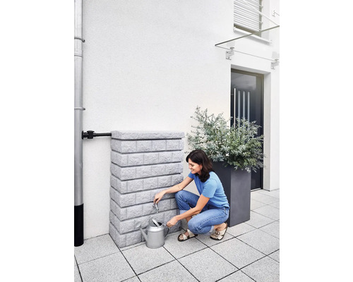 Vrouw vult gieter bij een regenwatertank in de tuin.