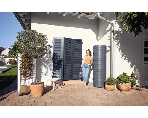 Tuinscene met regenton, huisdeur met luiken en vrouw met gieter