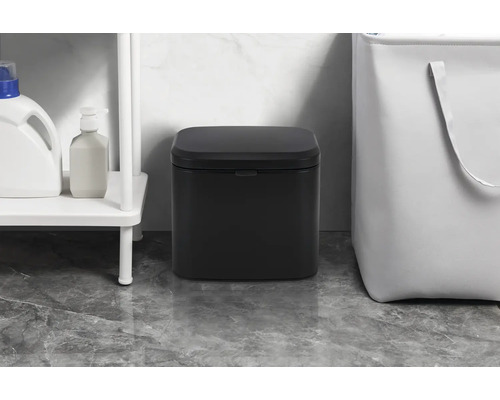 Zwarte pedaalemmer in de badkamer naast een plank en een wasmand.