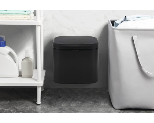 Wandafvalemmer naast een wasmand en een plank