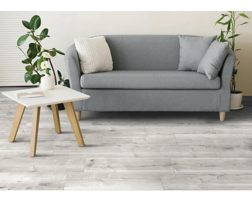 Lichte woonkamer met bank, tafel en houten tegelvloer.