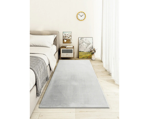 Slaapkamer met bed, nachtkastje en grijs tapijt op houten vloer.