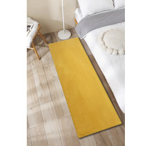 Geel tapijt in slaapkamer naast een bed, bijzettafel en staande lamp.