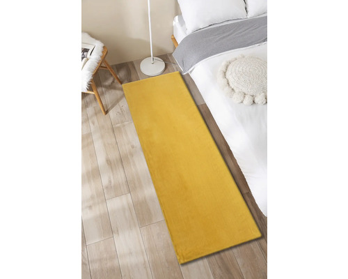 Geel tapijt in slaapkamer naast een bed, bijzettafel en staande lamp.