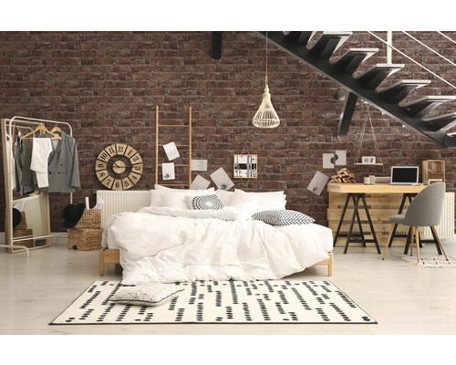 Slaapkamer met bed, bureau en trap tegen een bakstenen muur