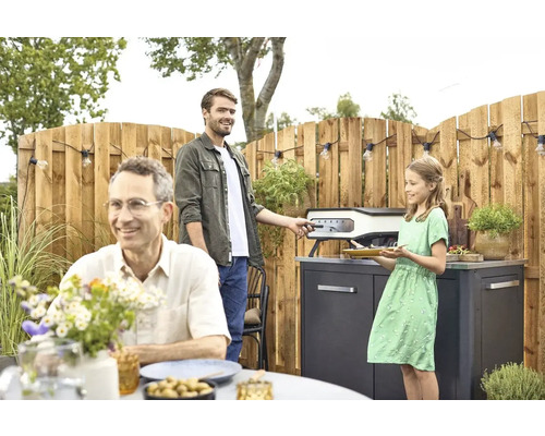 Familie bereidt eten met een pizzaoven in de tuin.
