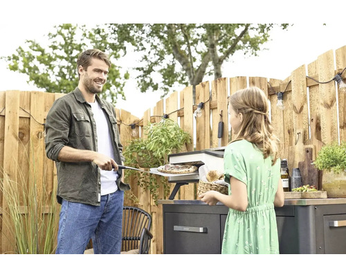 Man en meisje bereiden pizza in de buitenpizzaoven op het terras