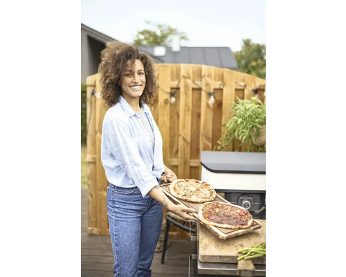 Vrouw houdt twee pizza''s vast in de tuin voor een pizzaoven