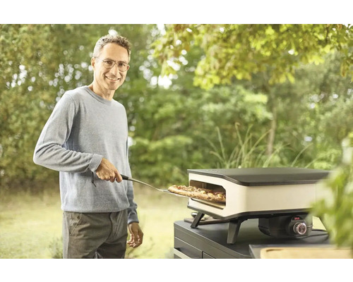 Een man schuift met een pizzaschep een pizza in een pizzaoven buiten.