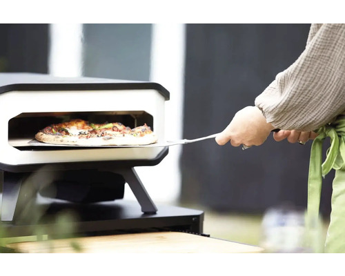 Pizza wordt met een pizzaschep uit een pizzaoven gehaald.