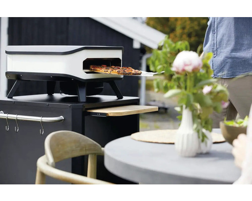 Pizzaoven op een tuintafel met pizza op een pizzaschep