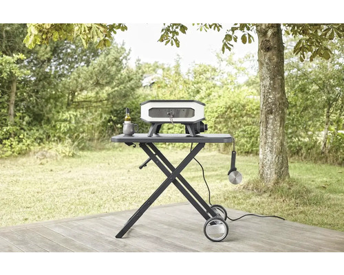 Pizzaoven op een rollende tafel in een tuin met olijfolie, mok en pizzasnijder